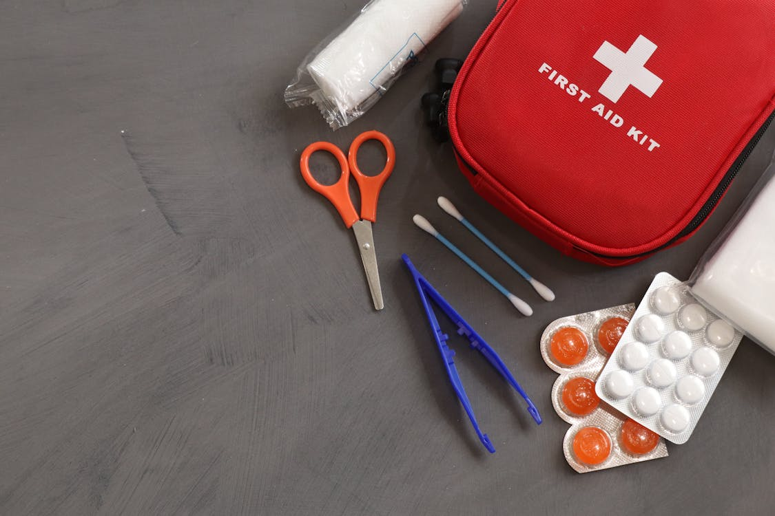 An image of a red first aid kit with cotton buds, scissors, tweezer, and medicines